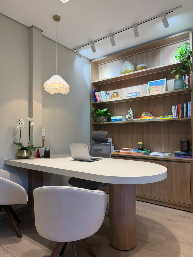 Mesa de atendimento com poltronas, luminária e estante de livros